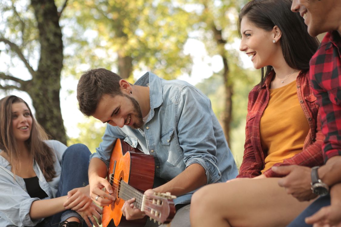 Friends laughing together while one plays an acoustic guitar outdoors